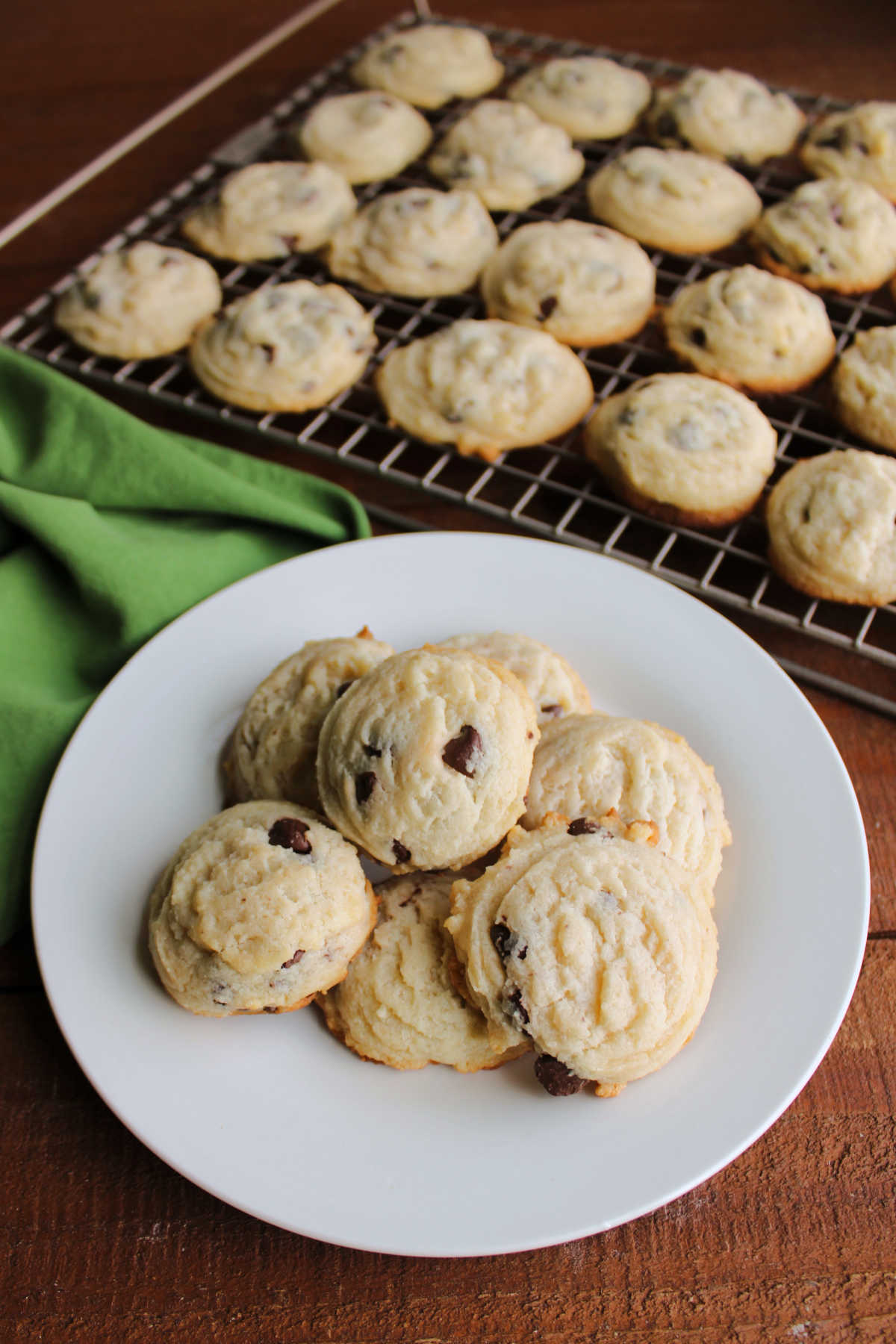 Plate of condensed milk cookies with chocolate chips near a wire rack with more cookies. 