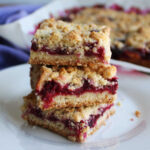 Three blackberry pie bars stacked on top of each other showing the crust layer, thick fruity filling and butter crumb topping.