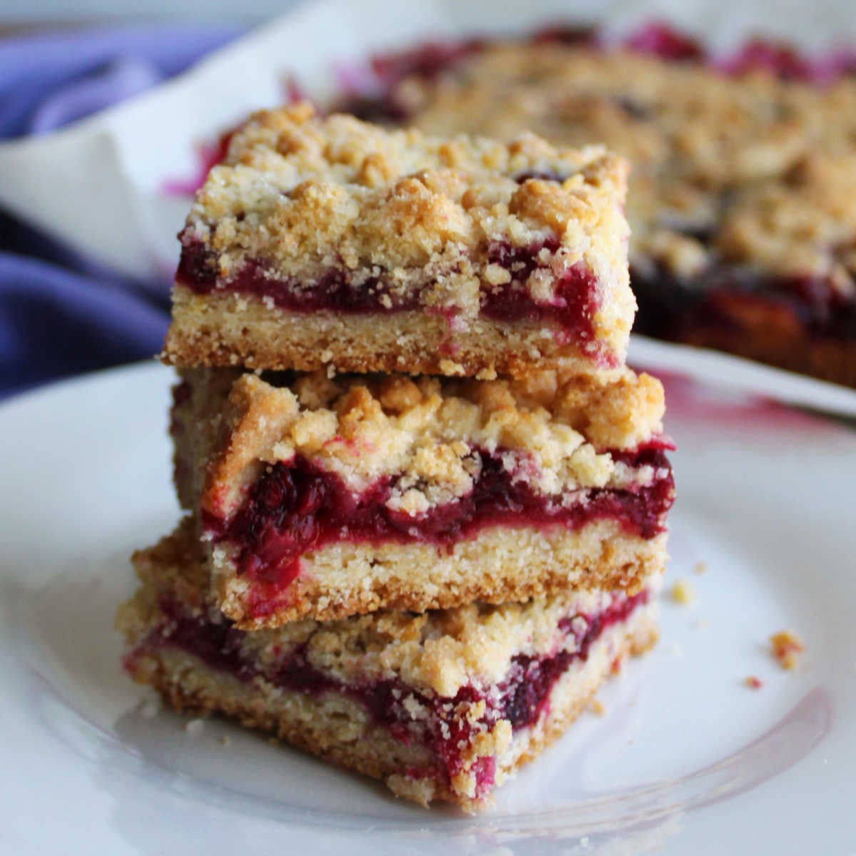 Blackberry Pie Bars 5 Three blackberry pie bars stacked on top of each other showing the crust layer, thick fruity filling and butter crumb topping.