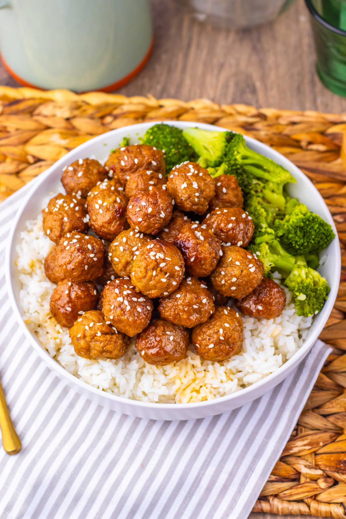 Plate of slow cooker Mongolian meatballs with brown sauce and sesame seeds served over rice with a side of broccoli. 