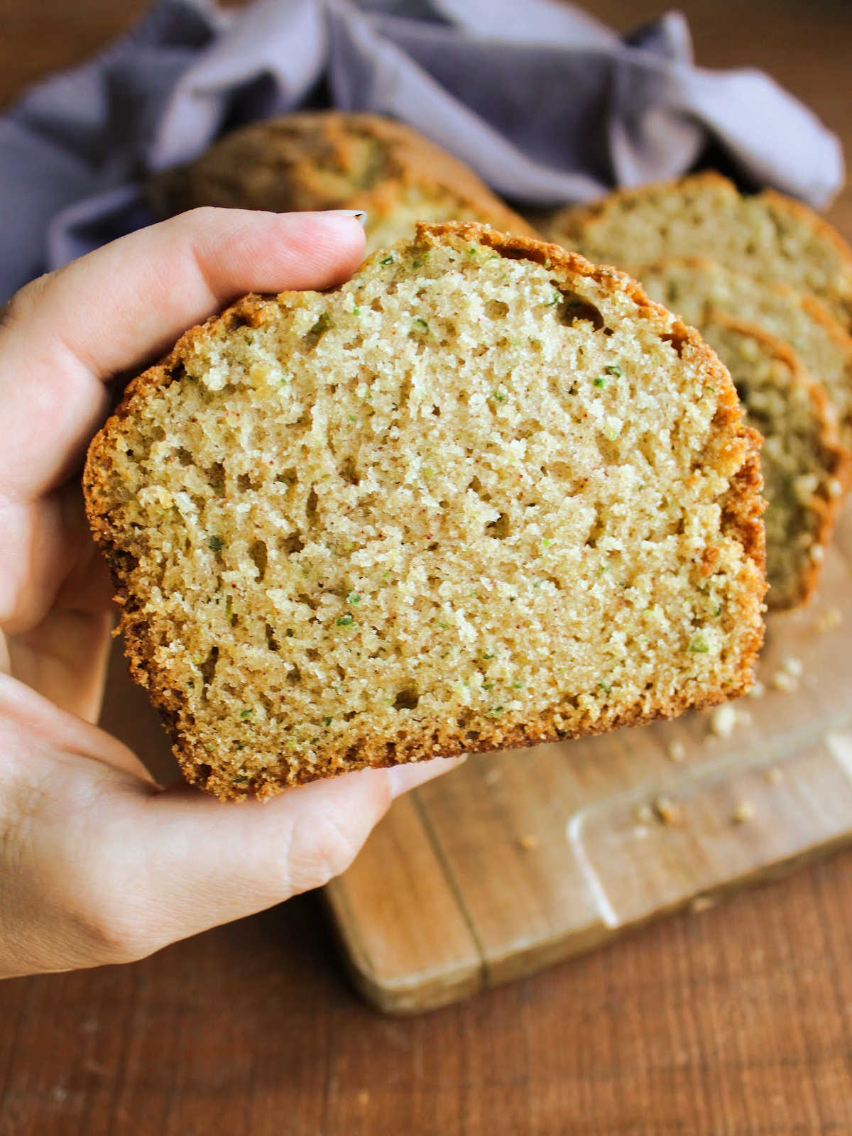 Hand holding a slice of cucumber bread with tiny flecks of green inside a tan bread, ready to eat. 