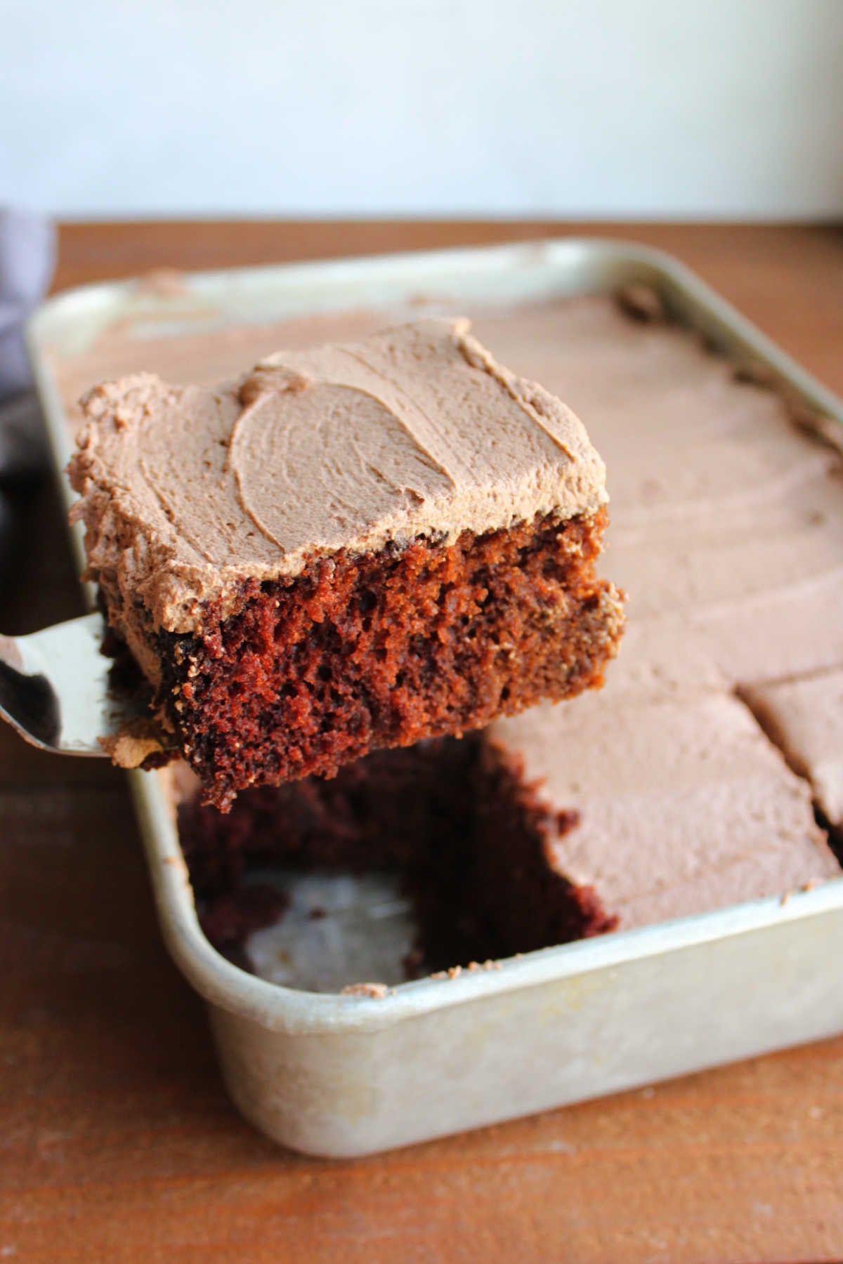 Spatula lifting piece of chocolate daffy cake out of the pan showing it's light and airy cake texture with a coating of chocolate frosting on top. 