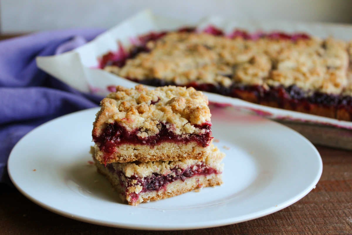 Blackberry Pie Bars 5 Two blackberry pie bars with crumble topping on small dessert plate with the remaining bars on a cutting board in the background.