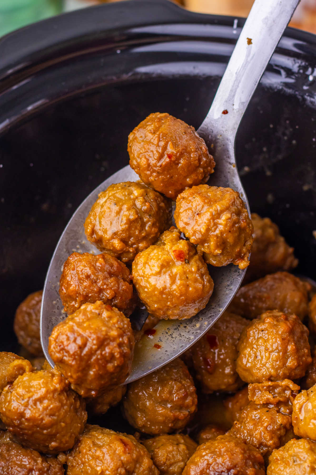 Serving spoon lifting a scoop of meatballs with thick Asian inspired sauce on them out of the crockpot they were cooked in. 
