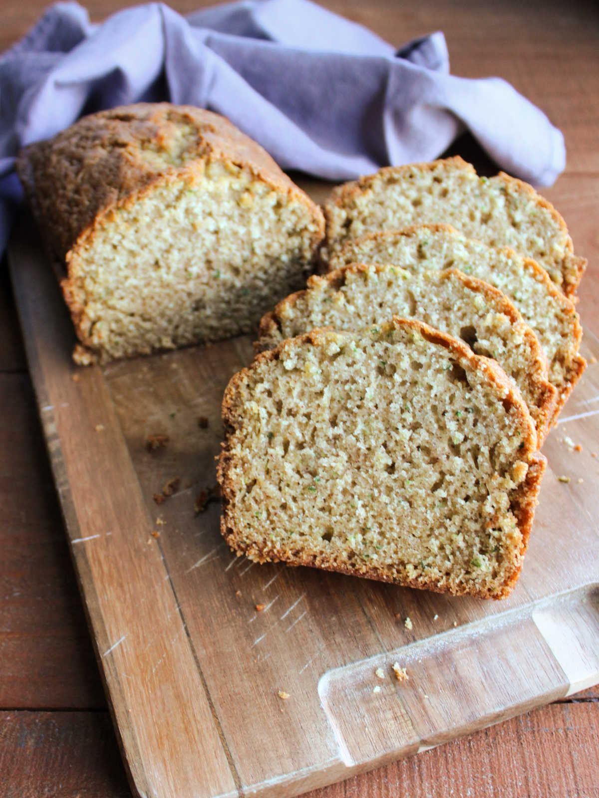 Loaf of cucumber bread being sliced on wooden cutting board showing soft texture inside with a slightly crunchy crust on top. 