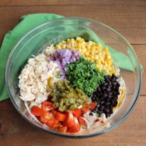 Diced chicken, corn, black beans, tomatoes, jalapeno, red onion, and cilantro being added to large mixing bowl with creamy taco dressing.