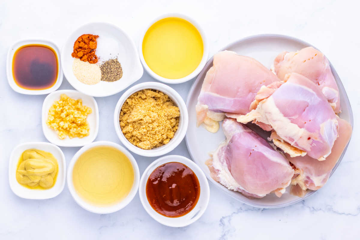 Ingredients including boneless skinless chicken thighs, bbq sauce, apple cider, Worcestershire sauce, apple cider vinegar and seasonings ready to go in the crockpot to make pulled chicken. 