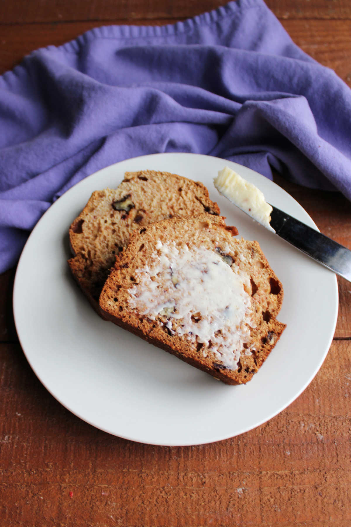 Grandma's Date Nut Bread 9 Smear of butter spread over a slice of date nut bread on plate, ready to eat.
