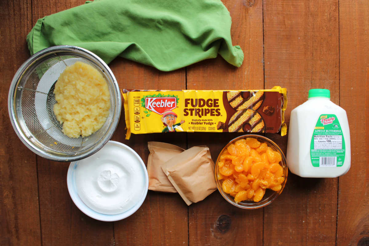 Ingredients including crushed pineapple, mandarin oranges, buttermilk, instant pudding mix, whipped topping, and fudge stripe cookies ready to be made into cookie salad. 