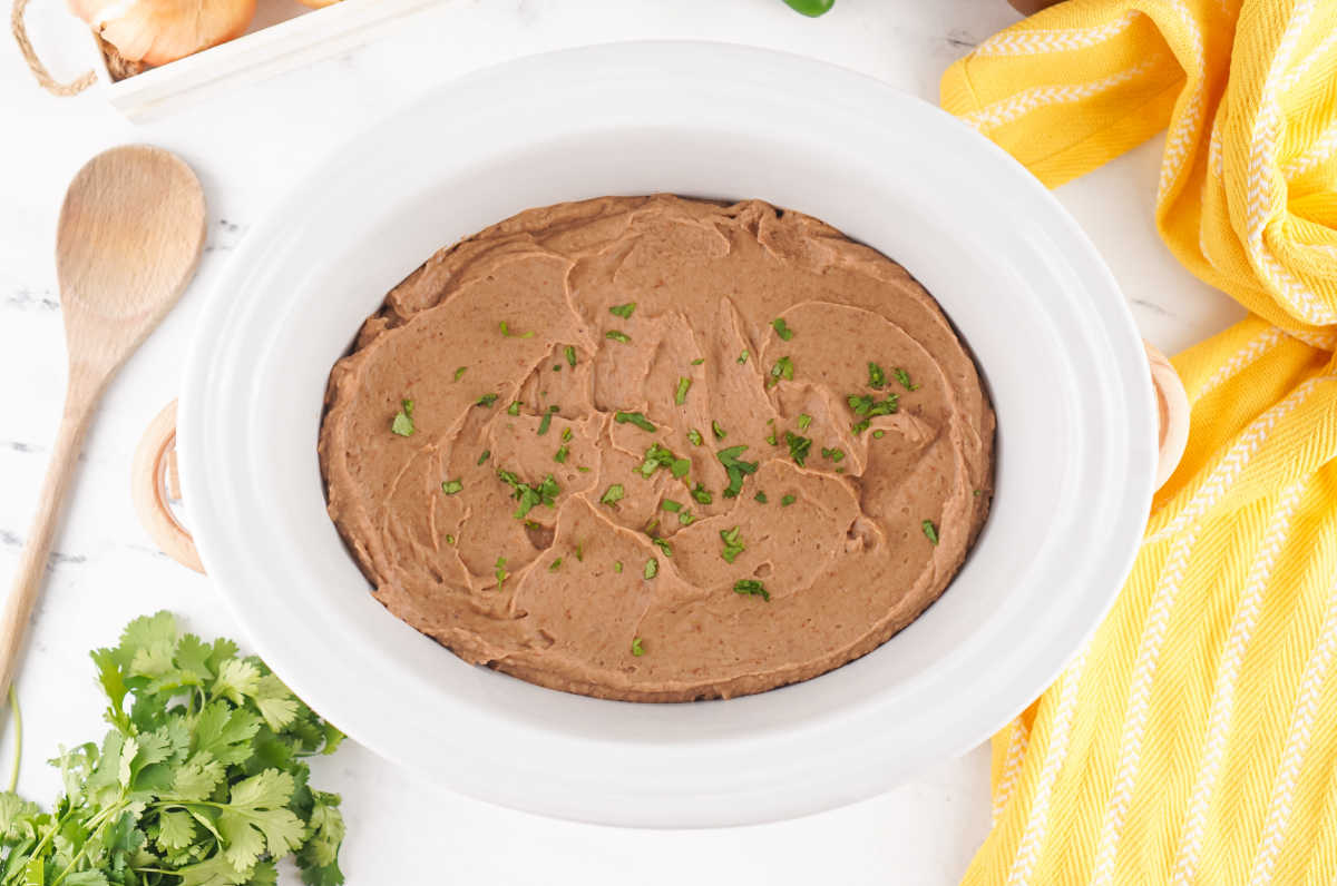 Slow cooker filled with creamy refried beans after they have been processed. 