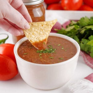 Hand dipping tortilla chip into a bowl of homemade restaurant style blender salsa.