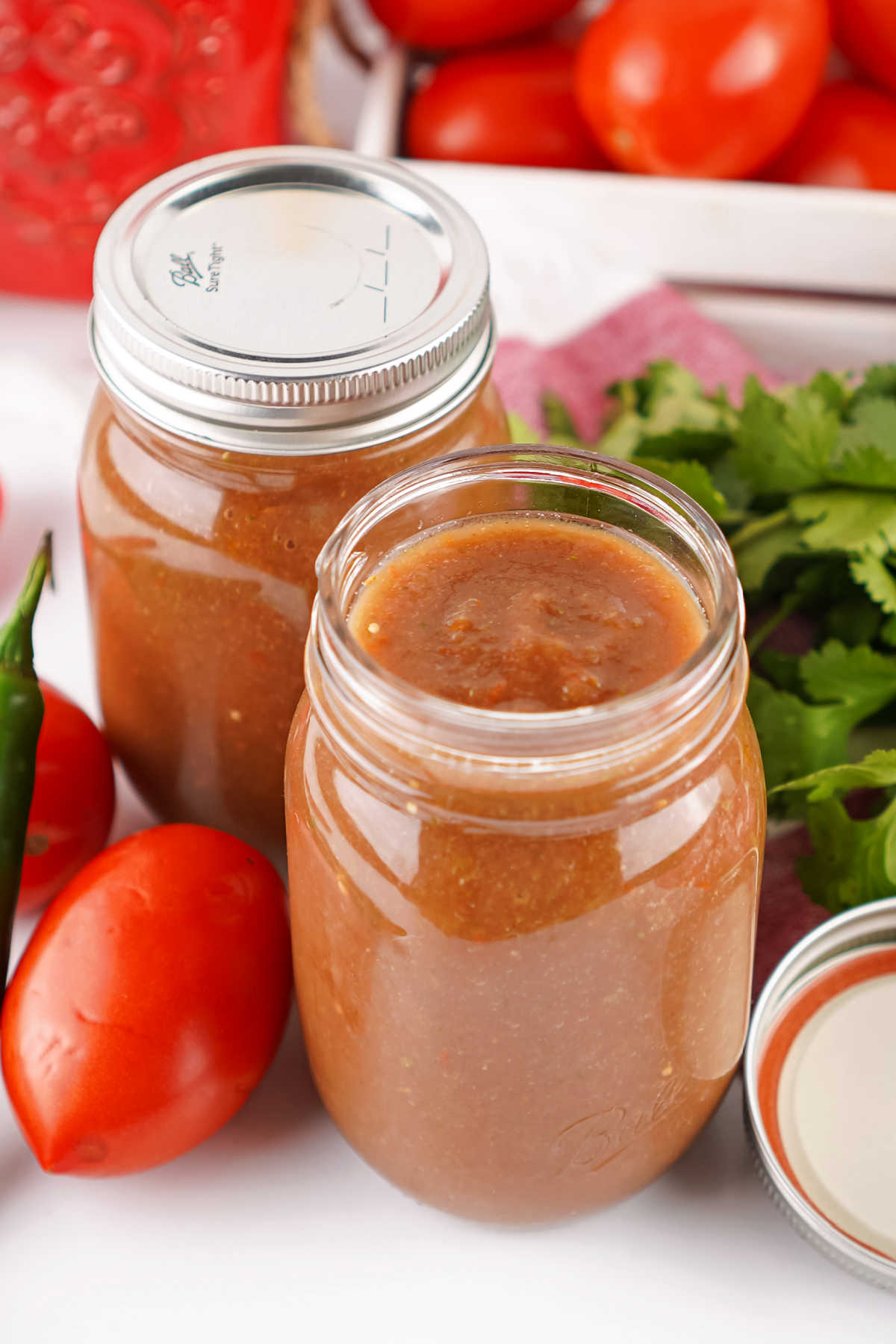 Jars of homemade restaurant style blender salsa with tomatoes, peppers, cilantro, and onions. 