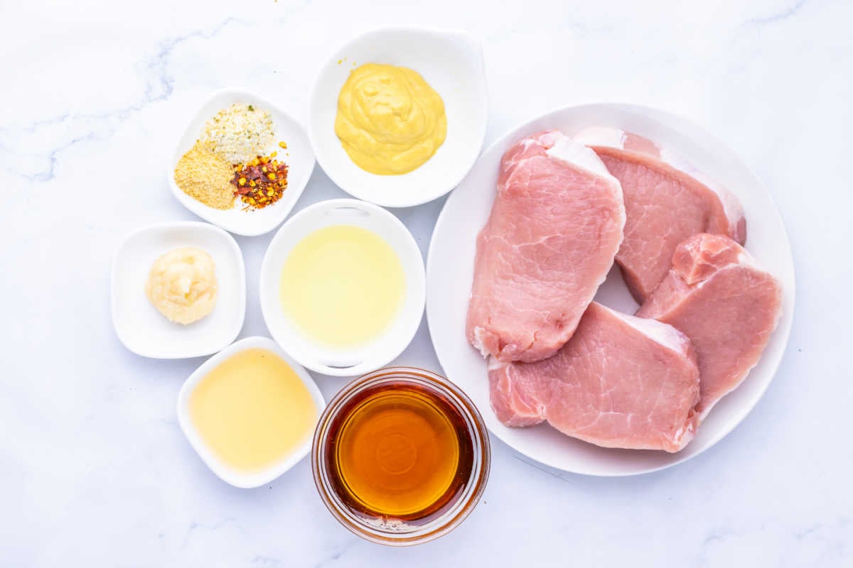 Ingredients including pork chops, maple syrup, dijon mustard, apple cider vinegar and seasonings ready to be made into maple dijon pork chops. 