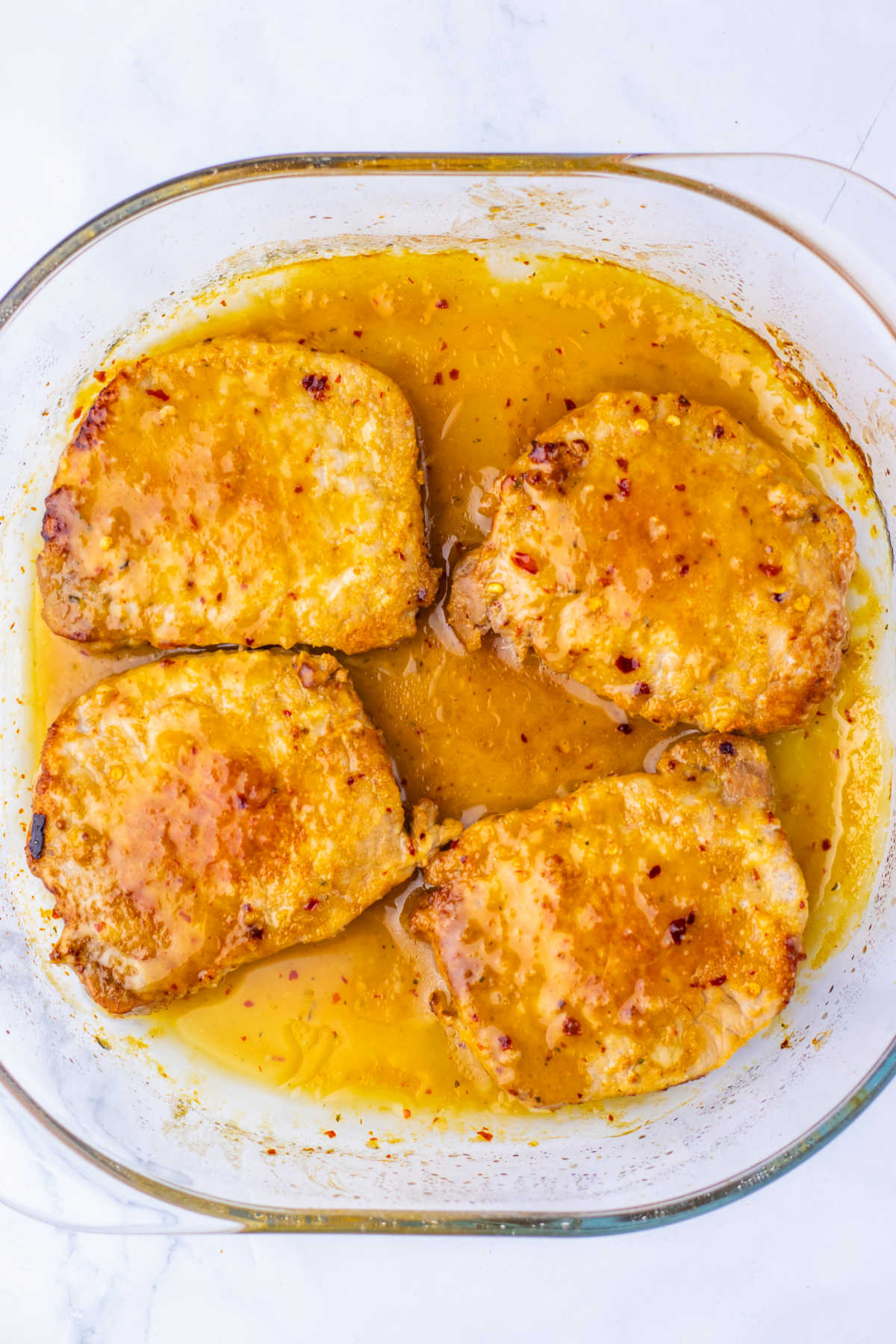 Square baking dish with four pork chops baked in a maple mustard sauce inside. 