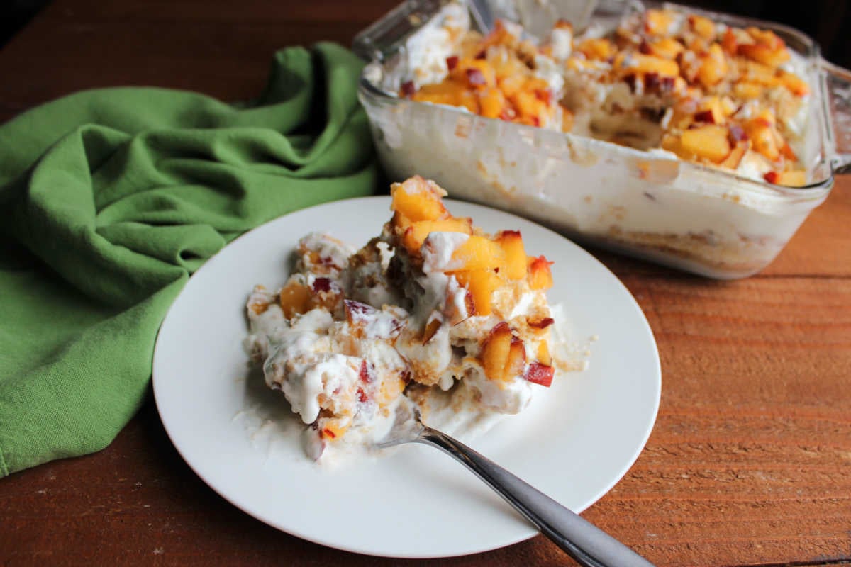 Peaches and Cream Icebox Cake 7 Fork getting a bite of peaches and cream refrigerator cake with layers of whipped cream, graham crackers, and peaches.
