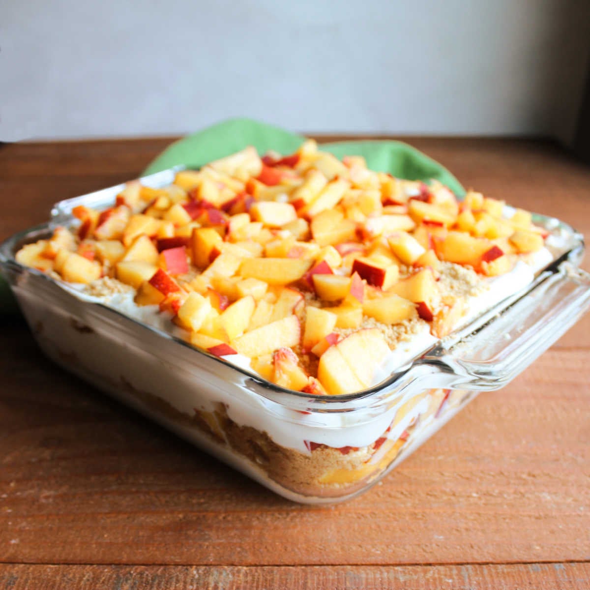 Peaches and Cream Icebox Cake 8 Square baking dish filled with layers of graham cracker crumbs whipped cream, and peaches to make a tasty peach icebox cake.