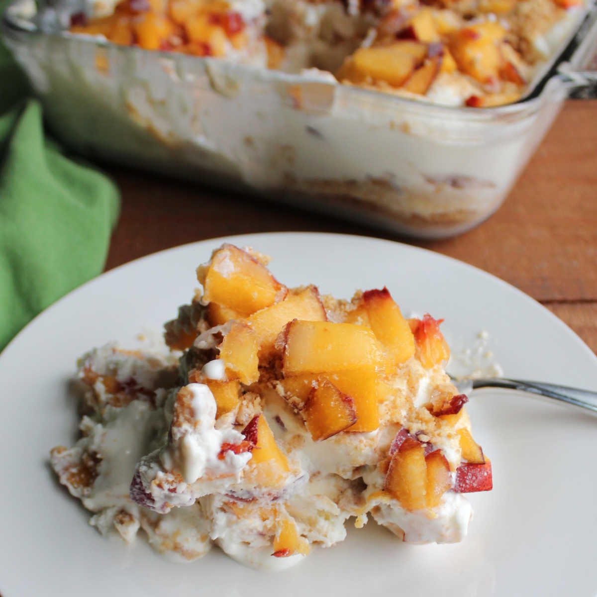 Peaches and Cream Icebox Cake 9 Close up of a pieces of peach refrigerator cake on plate showing fresh peaches with lots of whipped cream and graham cracker crumbs.