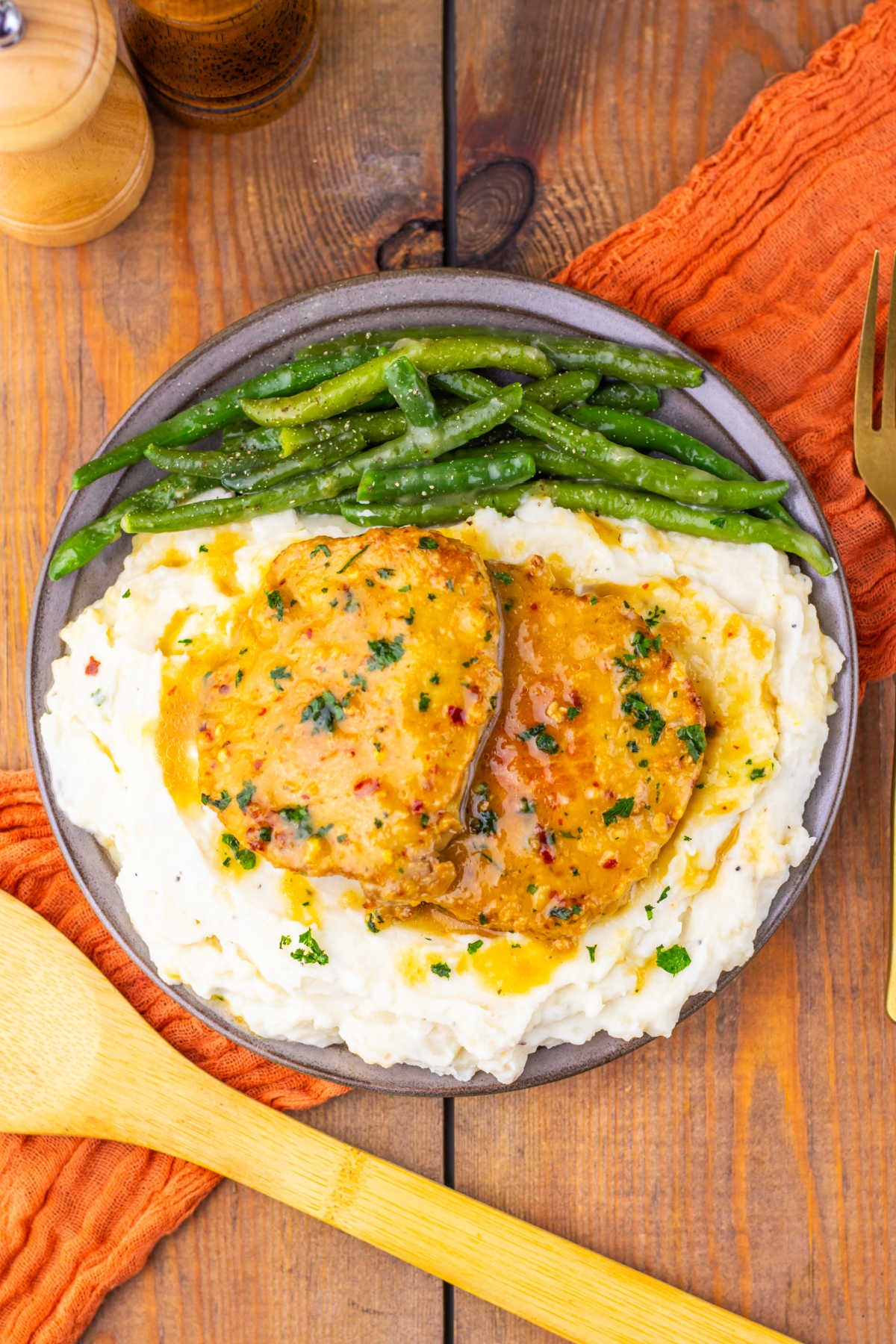 Dinner plate filled with mashed potatoes topped with pork chops coated in a mustard and maple sauce served with green beans, ready to eat. 