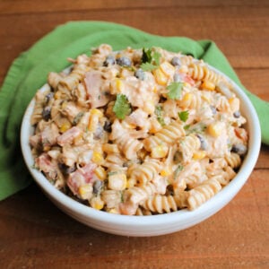 Serving bowl filled with pasta salad with creamy taco dressing, chunks of chicken, corn, black beans, tomatoes, onion, jalapeno and cilantro.