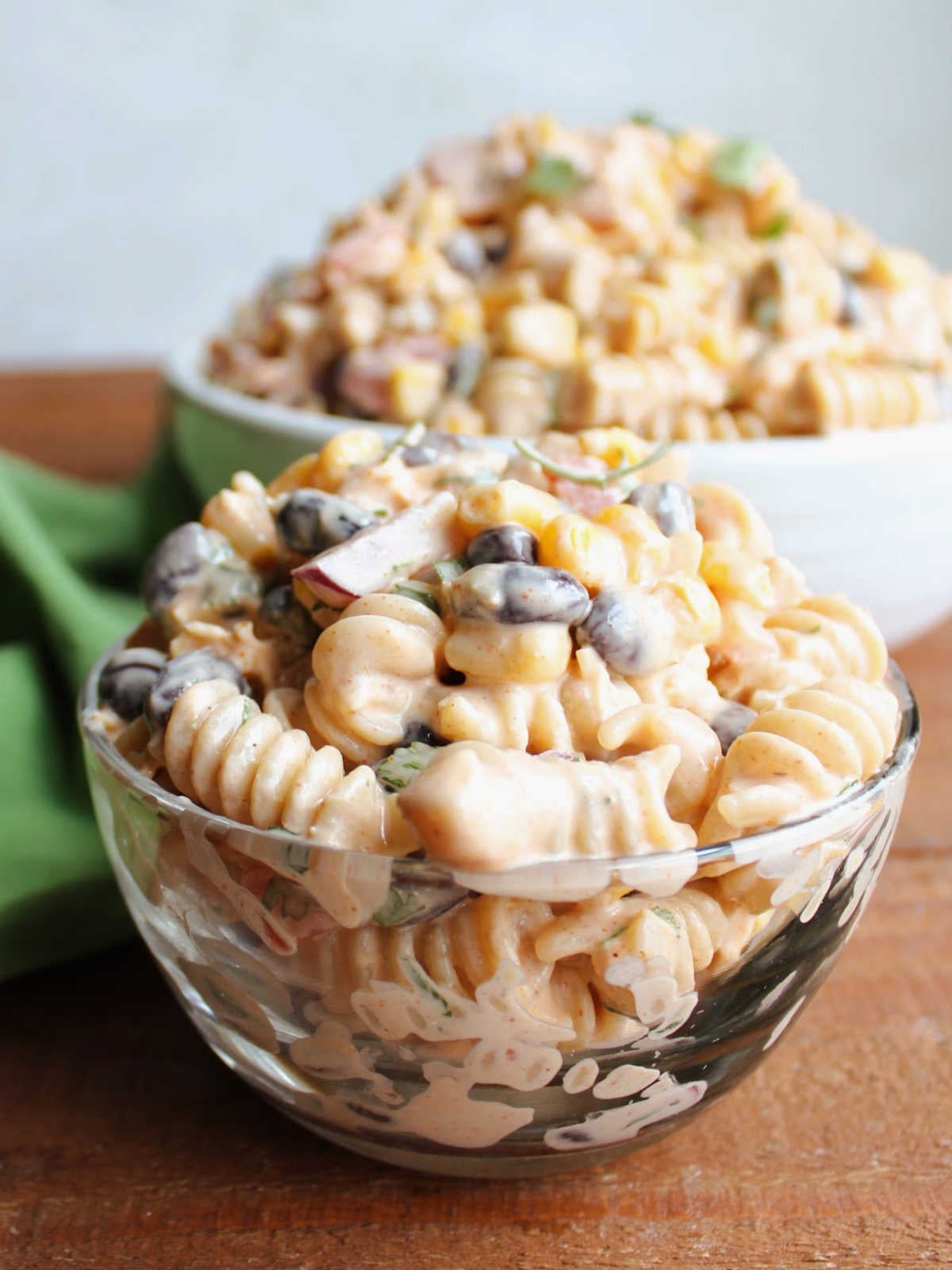 Small glass bowl filled with pasta salad in creamy taco dressing with rotini pasta, corn, black beans, tomatoes, onion, jalapeno and cilantro, ready to eat. 
