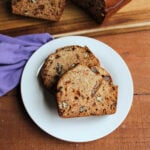 Two slice of date nut loaf on plate showing tan interior with slightly dense crumb, with bits of dates and nuts throughout.