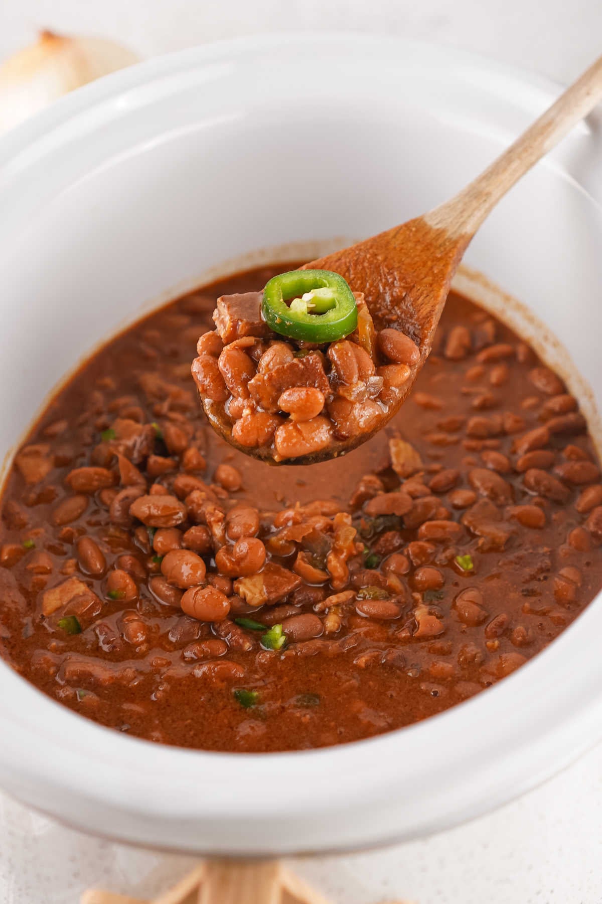 Crockpot Baked Beans With Dried Beans 8 Spoon getting a scoop of homemade baked beans out of a crockpot.
