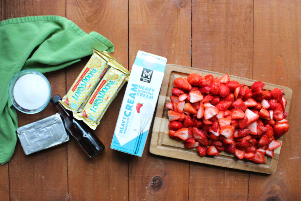 Ingredients including cream cheese, sugar, vanilla, shortbread cookies, heavy cream, and lots of fresh strawberries ready to be made into an icebox cake. 