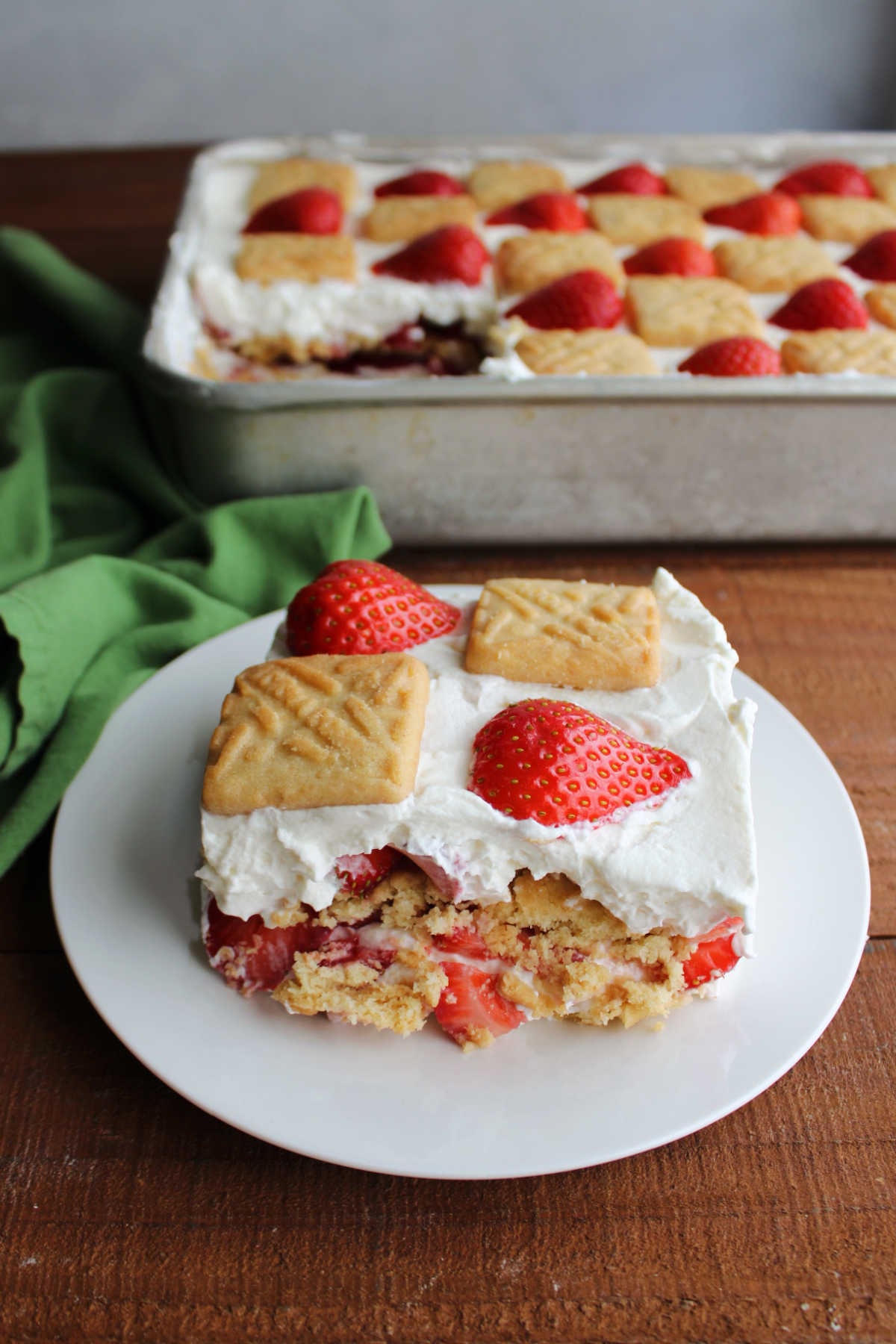 Piece of strawberry refrigerator cake on small plate with pan of more dessert in the background. 