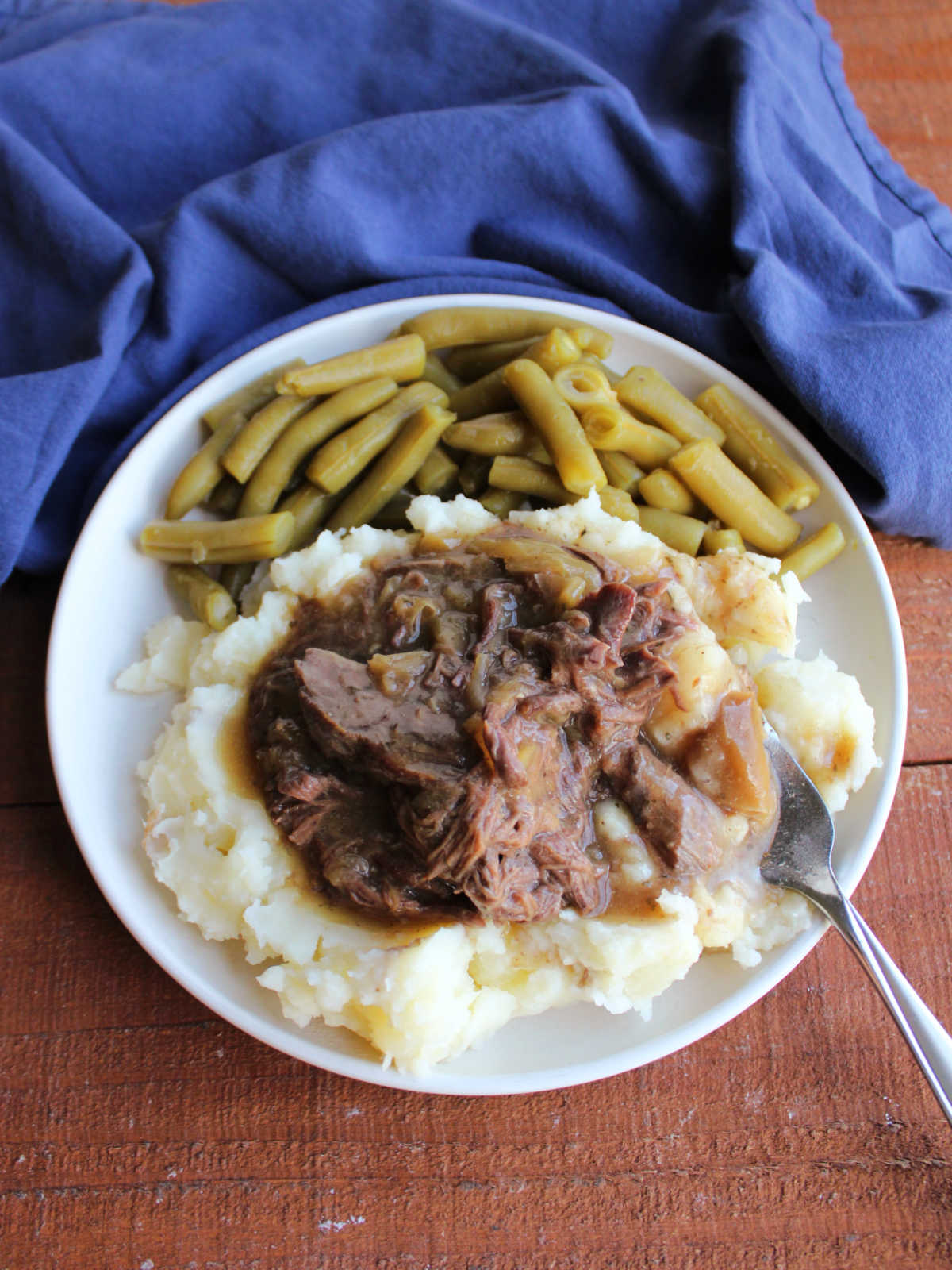 Bite of shredded deer meat in gravy with mashed potatoes on a fork, ready to eat. 