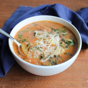 Spoon lifting up bite of soup with a gnocchi with bits of Italian sausage and spinach in a creamy tomato broth.