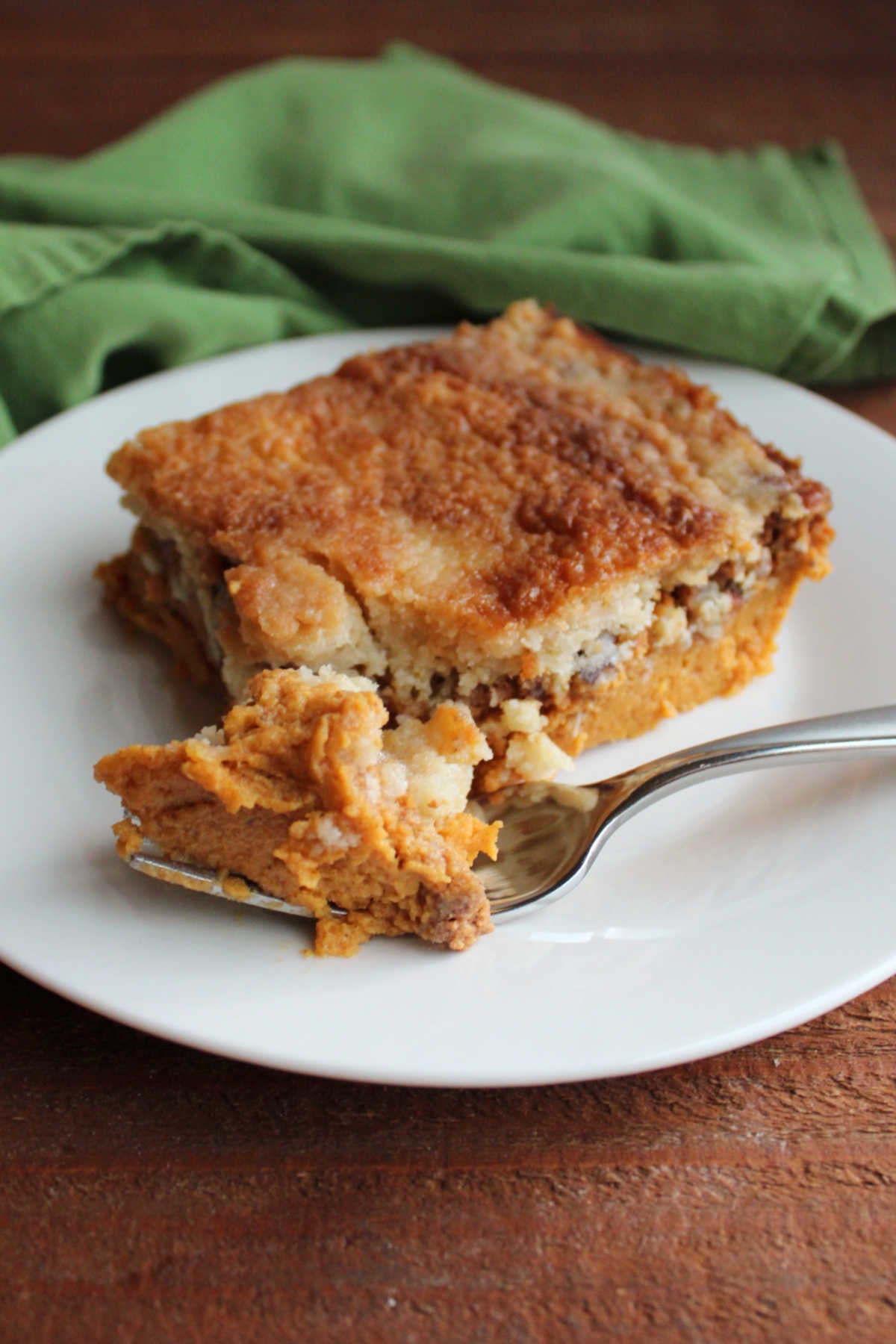 Fork getting a bite of pumpkin dump cake showing the thick layer of pumpkin pie like filling topped with buttery cake topping with bits of pecans. 
