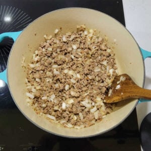 Large dutch oven with browned Italian sausage and diced onions inside.
