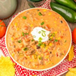 Bowl filled with creamy taco soup with ground beef, beans, corn, and tomatoes in cheesy broth topped with a dollop of sour cream and sliced green onions.