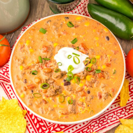 Creamy Crockpot Taco Soup 1 Bowl filled with creamy taco soup with ground beef, beans, corn, and tomatoes in cheesy broth topped with a dollop of sour cream and sliced green onions.