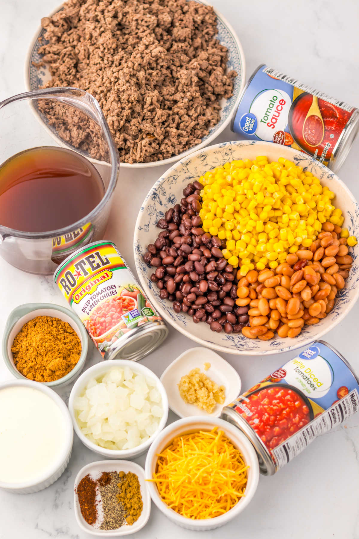 Ingredients including browned ground beef, corn, beans, Rotel, onion, diced tomatoes, seasonings, beef broth, cream, and cheese ready to be made into cheesy taco soup. 