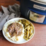 Dinner plate filled with green beans and smashed potatoes topped with venison roast in gravy with peppers, ready to eat.