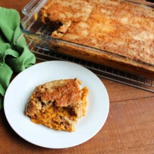Serving of pumpkin dump cake on plate with pan of remaining cake in the background showing golden brown topping.