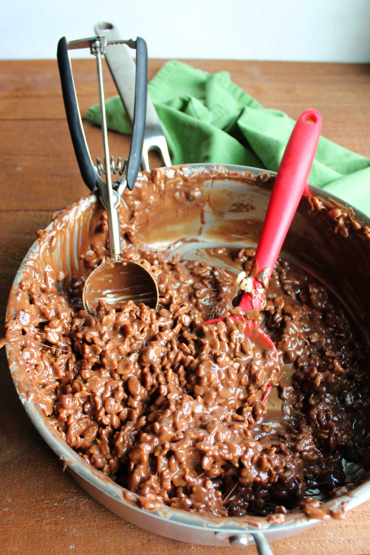 Homemade Star Crunch 8 Large sautee pan filled with gooey chocolate, caramel, marshmallow and cereal mixture with a spatula and a large cookie scoop.