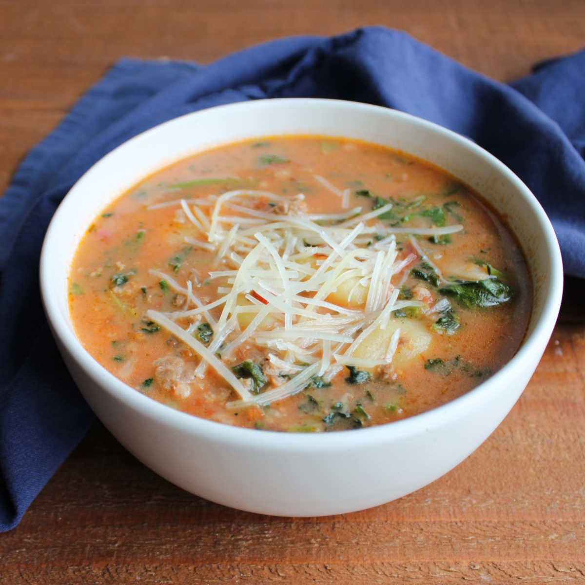 Close up of a bowl of creamy tomato soup with Italian sausage, spinach and gnocchi topped with parmesan cheese. 