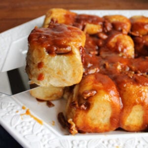 Spatula lifting a fluffy roll coated in butterscotch caramel roll with pecans, ready to be served.