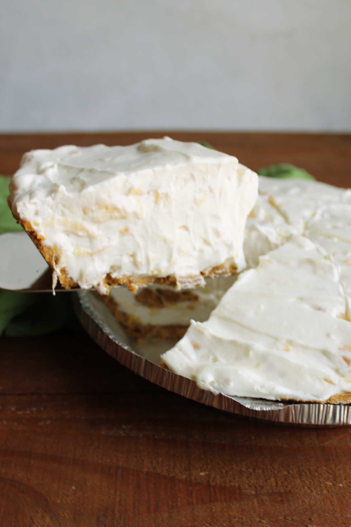 Lifting a slice of creamy pineapple pie out of the pan to serve it. 