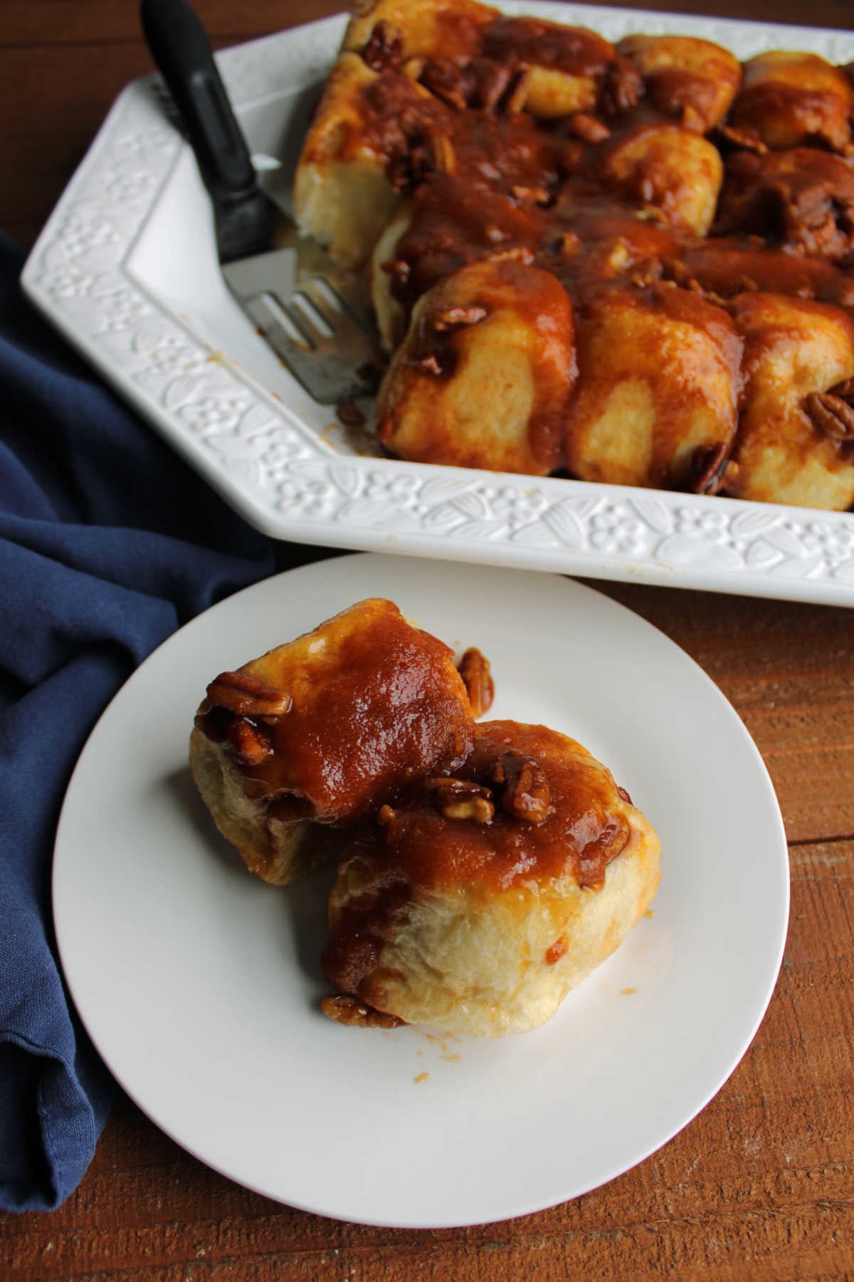Plate with a couple of freshly baked overnight butterscotch rolls with caramel coating and pecans, ready to eat. 