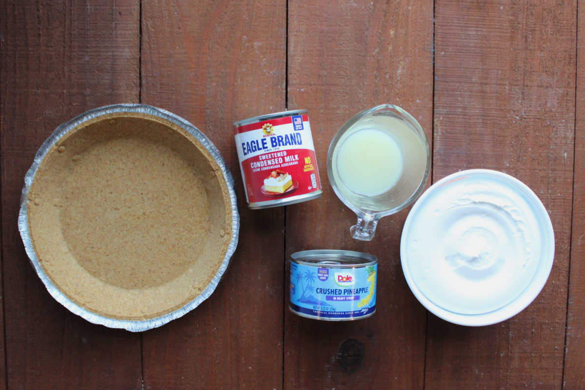 Ingredients including graham cracker crust, sweetened condensed milk, crushed pineapple, lemon juice, and whipped topping ready to be made into no bake pineapple pie. 