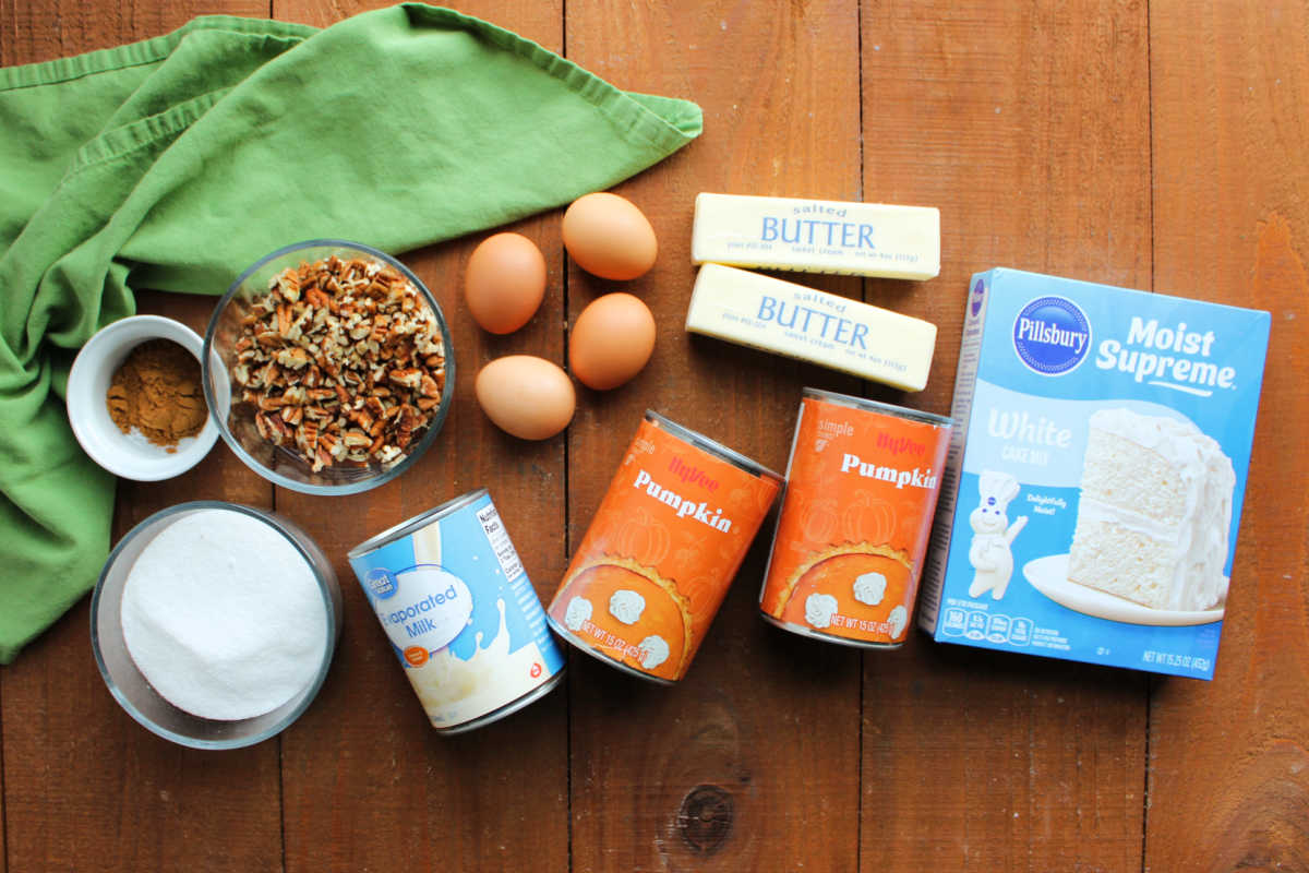 Ingredients including pumpkin puree, cake mix, butter, eggs, evaporated milk, pecans, sugar, and pumpkin pie spice ready to be made into a pumpkin dump cake. 