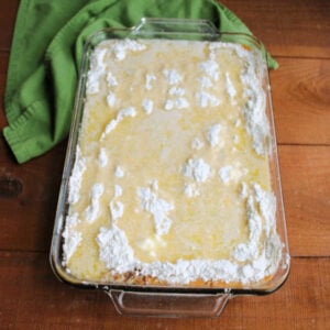 Pan of pumpkin dump cake ready to go in the oven showing dry cake mix topped with melted butter on top of the pumpkin mixture.