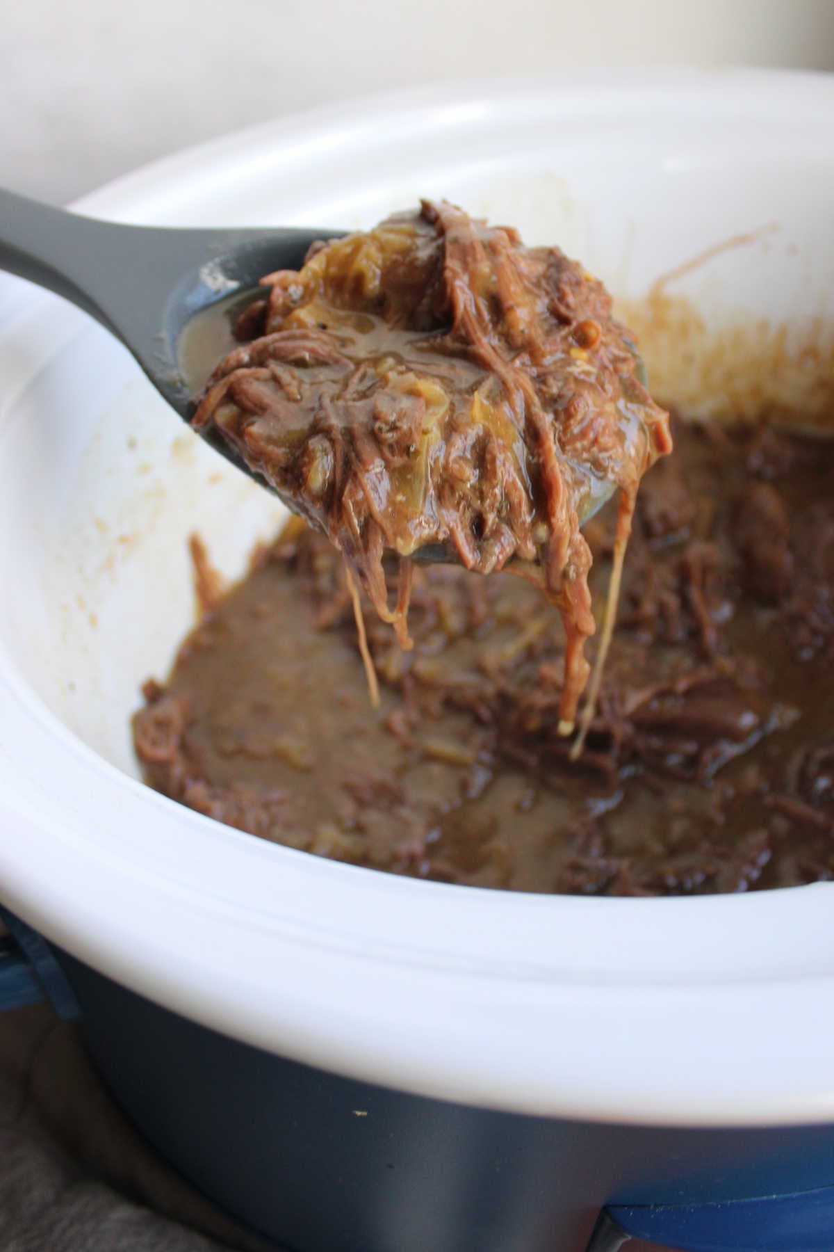 Serving spoon getting a scoop of shredded venison in a gravy with bits of pickled peppers, ready to be served. 