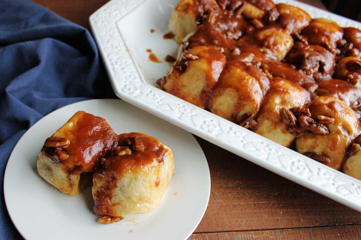Plate with two caramel rolls with fluffy bread base and cinnamon caramel coating with pecans, ready to eat. 