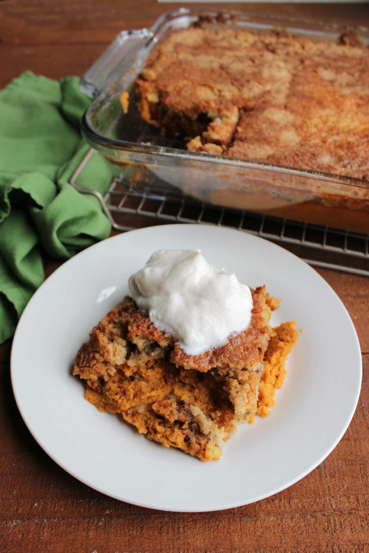 Pan of pumpkin dump cake next to a plate with a serving topped with whipped cream. 