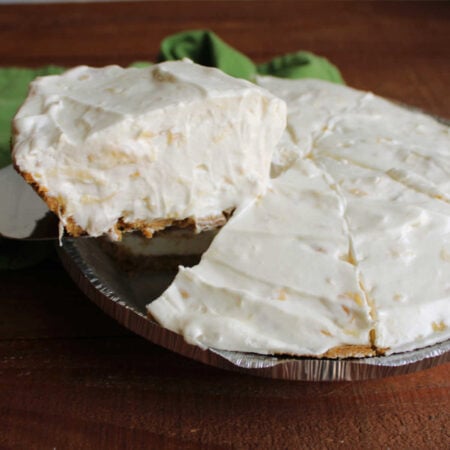 Creamy No Bake Pineapple Pie 1 Pie serving lifting slice of creamy no bake pineapple pie out of the pan showing airy filling with lots of little bits of pineapple throughout.