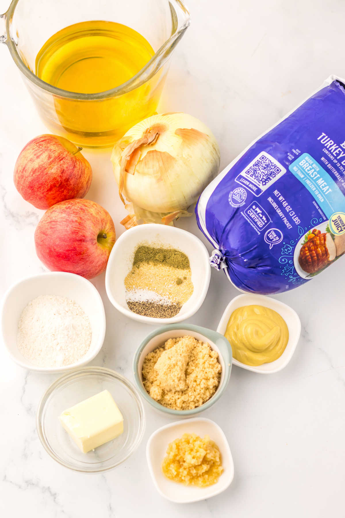 Ingredients including a boneless turkey breast, apple cider, apples, an onion, garlic, butter, mustard, and seasonings ready to go into a slow cooker. 